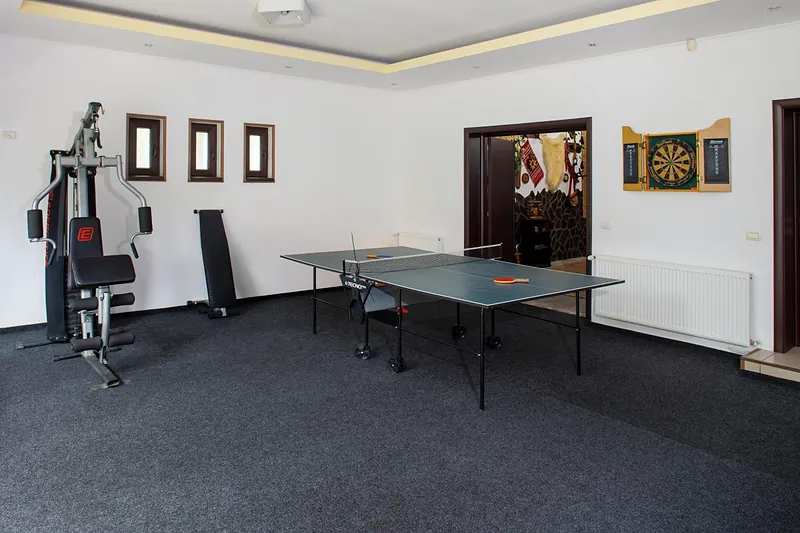 Sală cu aparat de fitness, masă de ping-pong și darts